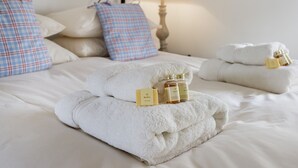 Cama bem arrumada com toalhas brancas e artigos de higiene pessoal, uma luminária e almofadas xadrez.
