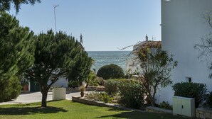 En ejendom ved kysten med en hvid bygning, en have med forskellige planter og udsigt til havet.