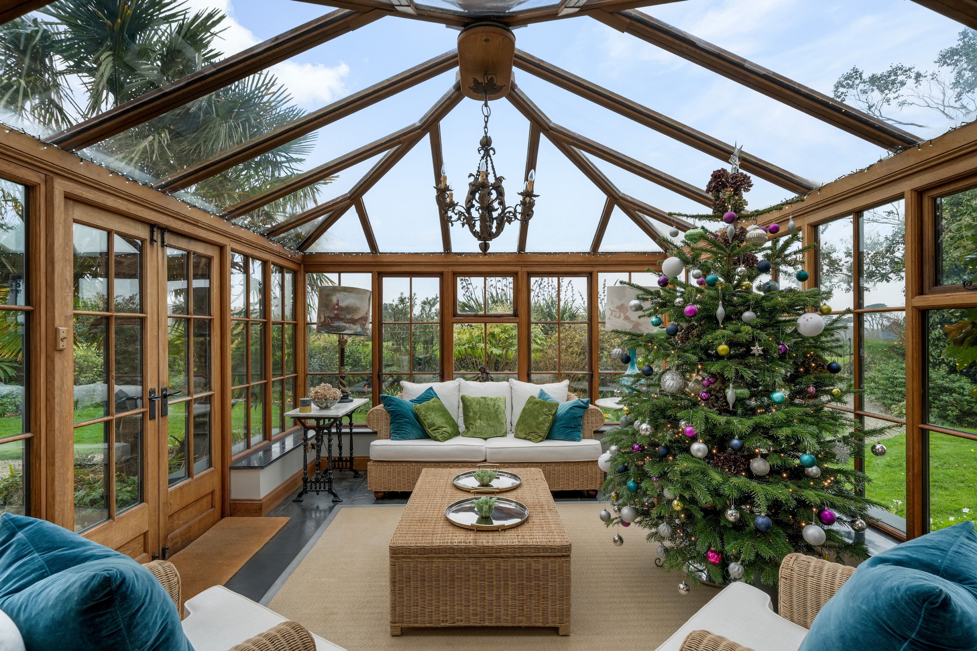 A conservatory with a glass ceiling, a Christmas tree, and a sofa with cushions.