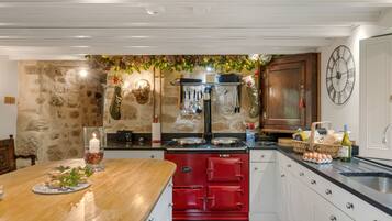 Una cocina con pared de piedra, estufa roja, armarios blancos, barra de madera y un reloj de pared.
