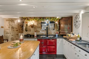 A kitchen with a stone wall, a red stove, white cabinets, a wooden bar counter, and a wall-mounted clock.