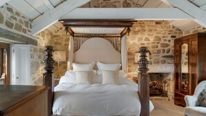 A four-poster canopy bed with white bedding, a stone wall, and a fireplace.