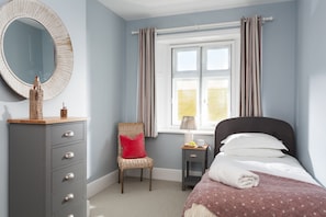A bedroom with a bed, a dresser, a chair, a window with curtains, and a lamp.