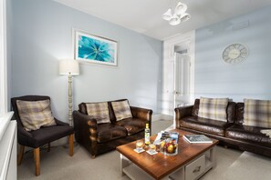A living room with two brown leather sofas, a wooden coffee table, a floor lamp, and a painting on the wall.
