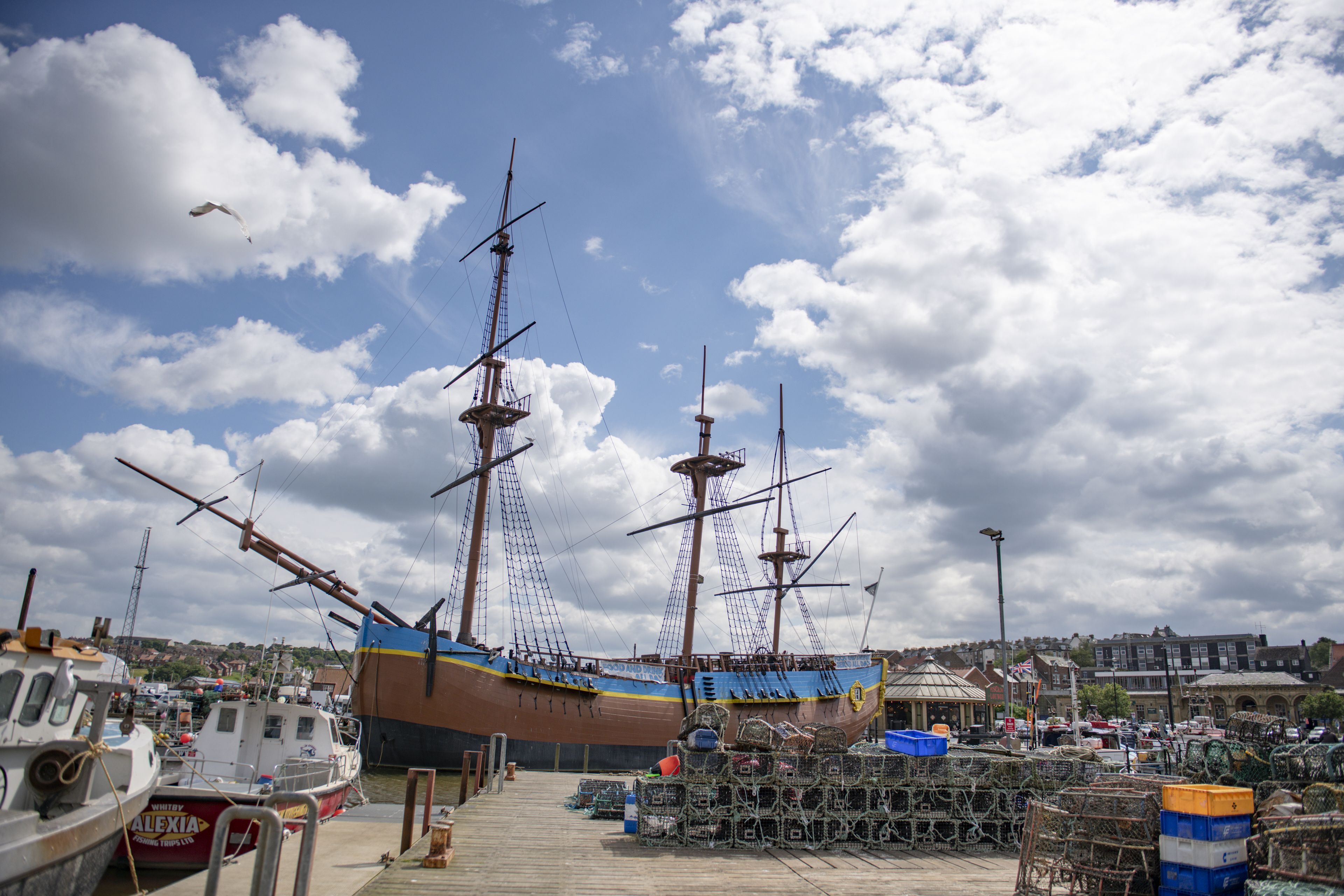 Eine Anlegestelle mit einem großen Segelschiff, kleineren Booten und einer Pier mit Angelausrüstung.