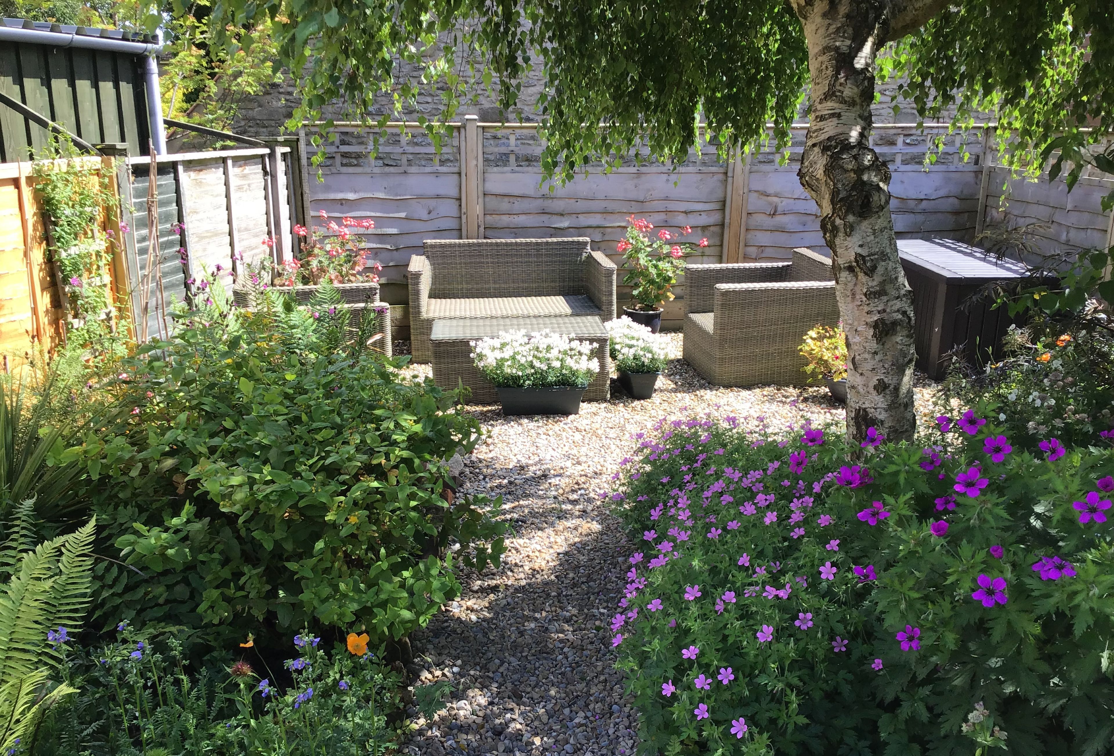 An outdoor seating area with wicker furniture, surrounded by a variety of plants and flowers.