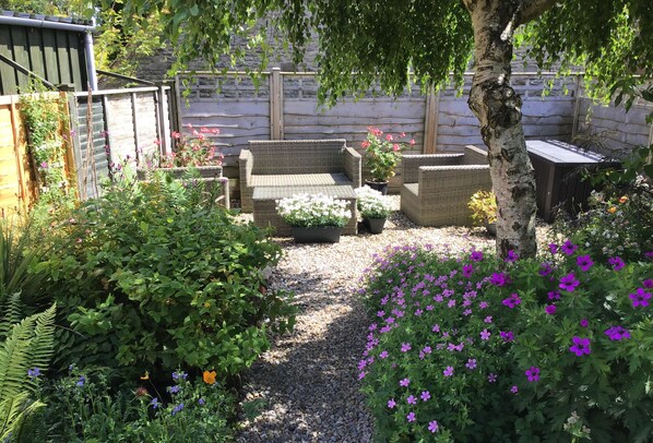 An outdoor seating area with wicker furniture, surrounded by a variety of plants and flowers.