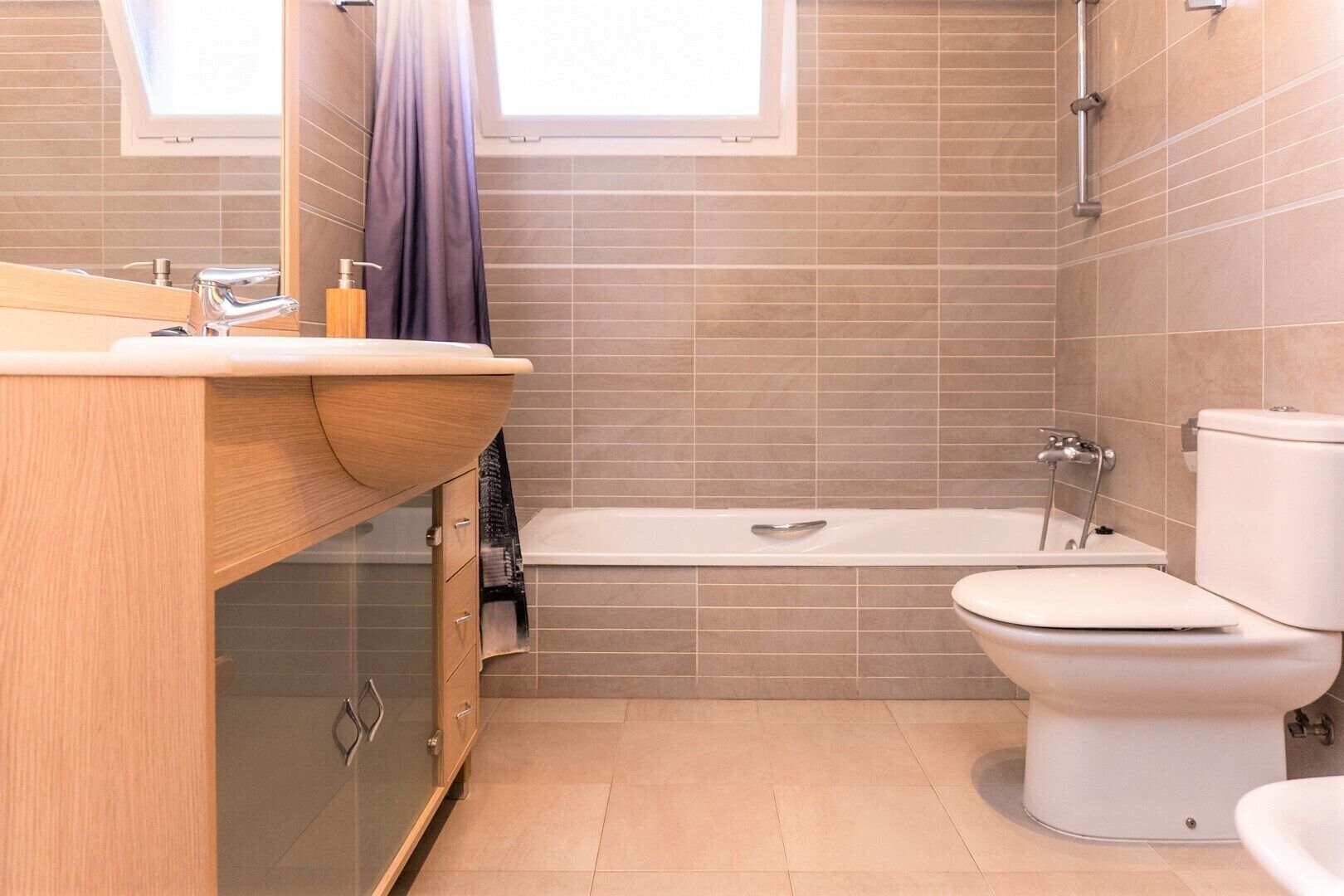 Une salle de bain avec un meuble-lavabo en bois, une baignoire et des toilettes.