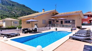 A swimming pool with lounge chairs and umbrellas, surrounded by a white fence, with a mountain in the background. - CHALET MONTESOL, LUXURY IN THE BEST AREA OF LA DROVA, NEXT TO GANDIA (barx)
