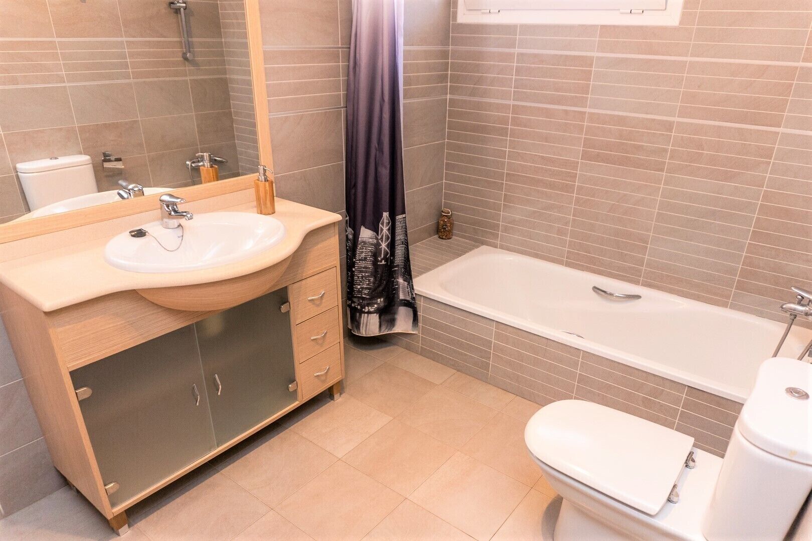 Een moderne badkamer met een houten wastafelmeubel, een witte wasbak, een badkuip en een toilet.