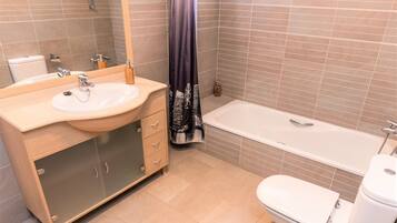Een moderne badkamer met een houten wastafelmeubel, een witte wasbak, een badkuip en een toilet.