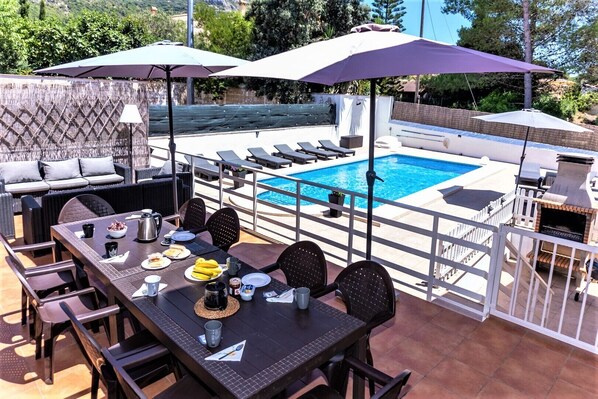A poolside dining area with a table set for two, surrounded by lounge chairs and umbrellas. - CHALET MONTESOL, LUXURY IN THE BEST AREA OF LA DROVA, NEXT TO GANDIA (barx)