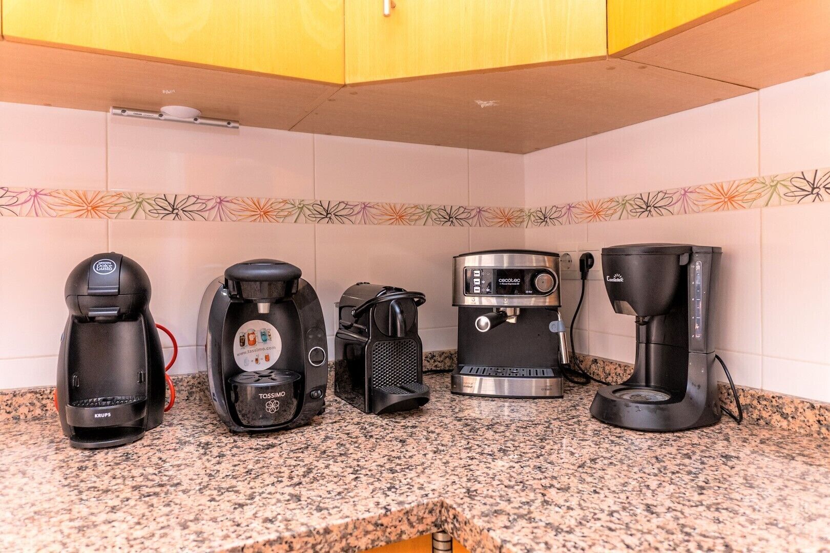 Una cocina con cuatro cafeteras sobre una encimera de granito.