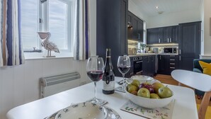 Uma cozinha moderna com armários escuros, bancada branca e um espaço de jantar com mesa posta para dois.