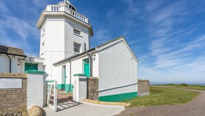 Um farol branco com porta verde e uma pequena escadaria que leva à entrada.