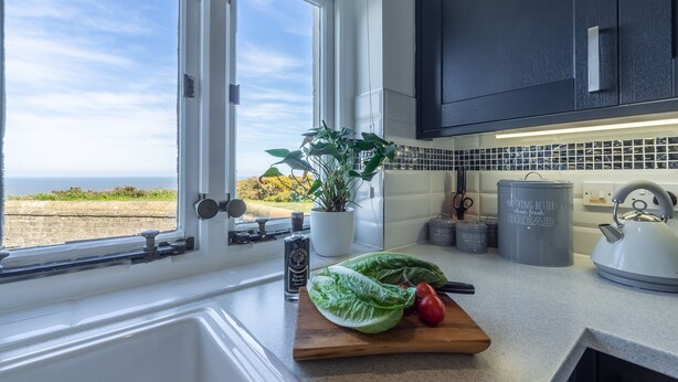 Cozinha com vista para o mar, um vaso de planta, uma tábua de corte com legumes e uma chaleira.