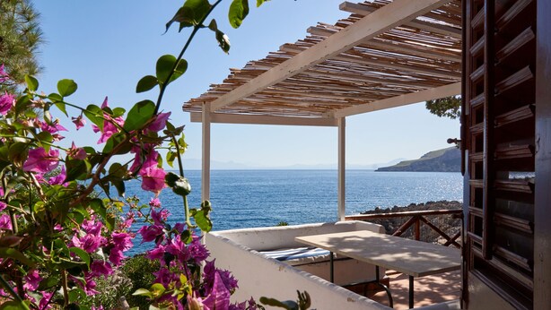A covered outdoor seating area with a view of the sea and mountains.