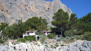 A mountainous landscape with a white building featuring balconies, surrounded by trees and rocky terrain.