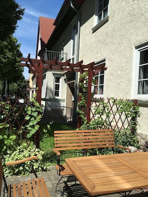 A wooden bench and table set in a garden area with a pergola and climbing plants.