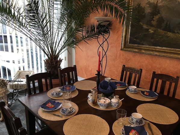A dining table set with blue and white patterned tableware, a red candle, and a large potted plant.