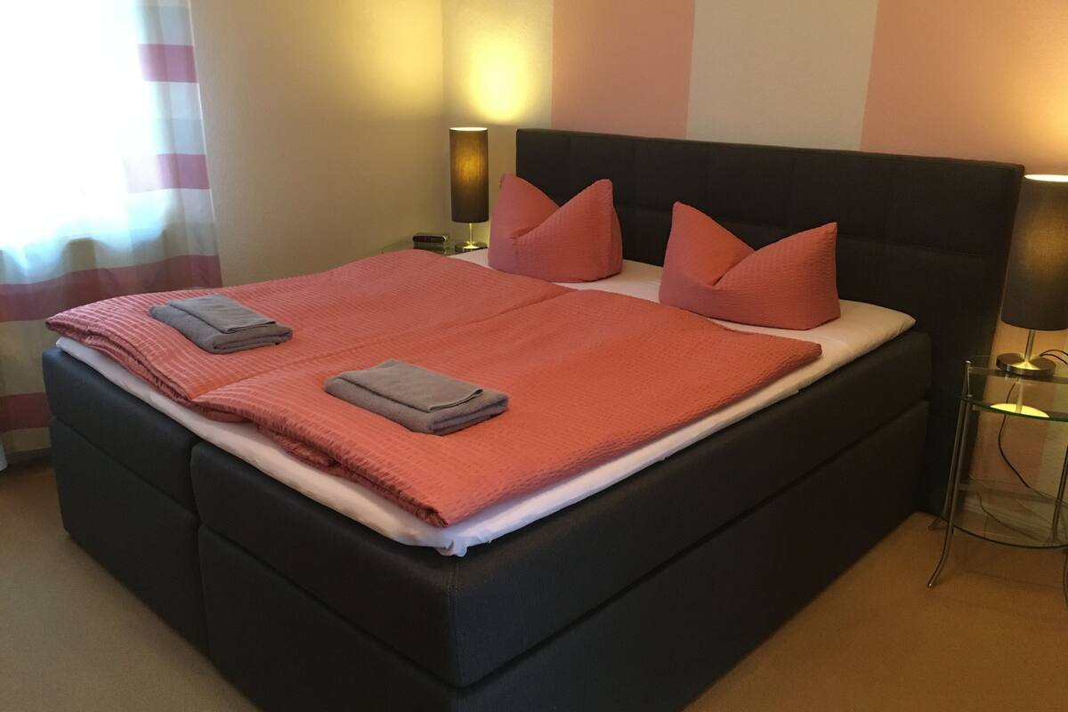 A neatly made bed with a pink and white striped bedspread, two pillows, and a folded towel.