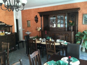 A dining area with a wooden table set for four, surrounded by chairs. A large wooden cabinet with glass doors is against the wall. - Pension Wegerich (Erfurt)