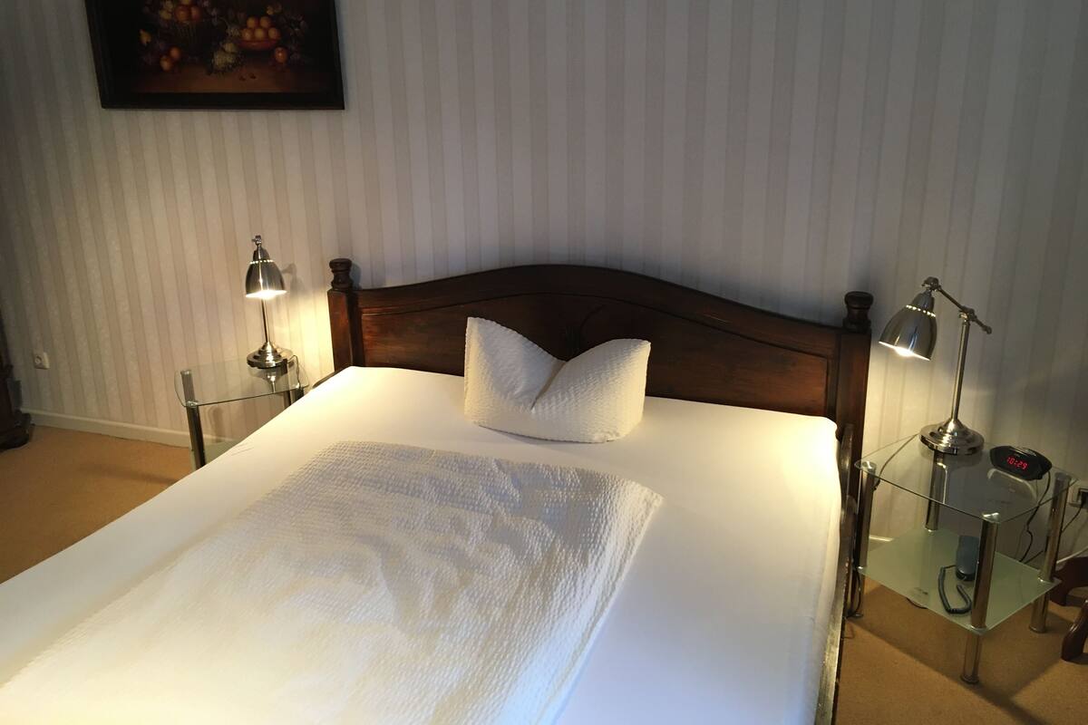 A neatly made bed with white linens, two bedside lamps, and a digital clock on a bedside table.