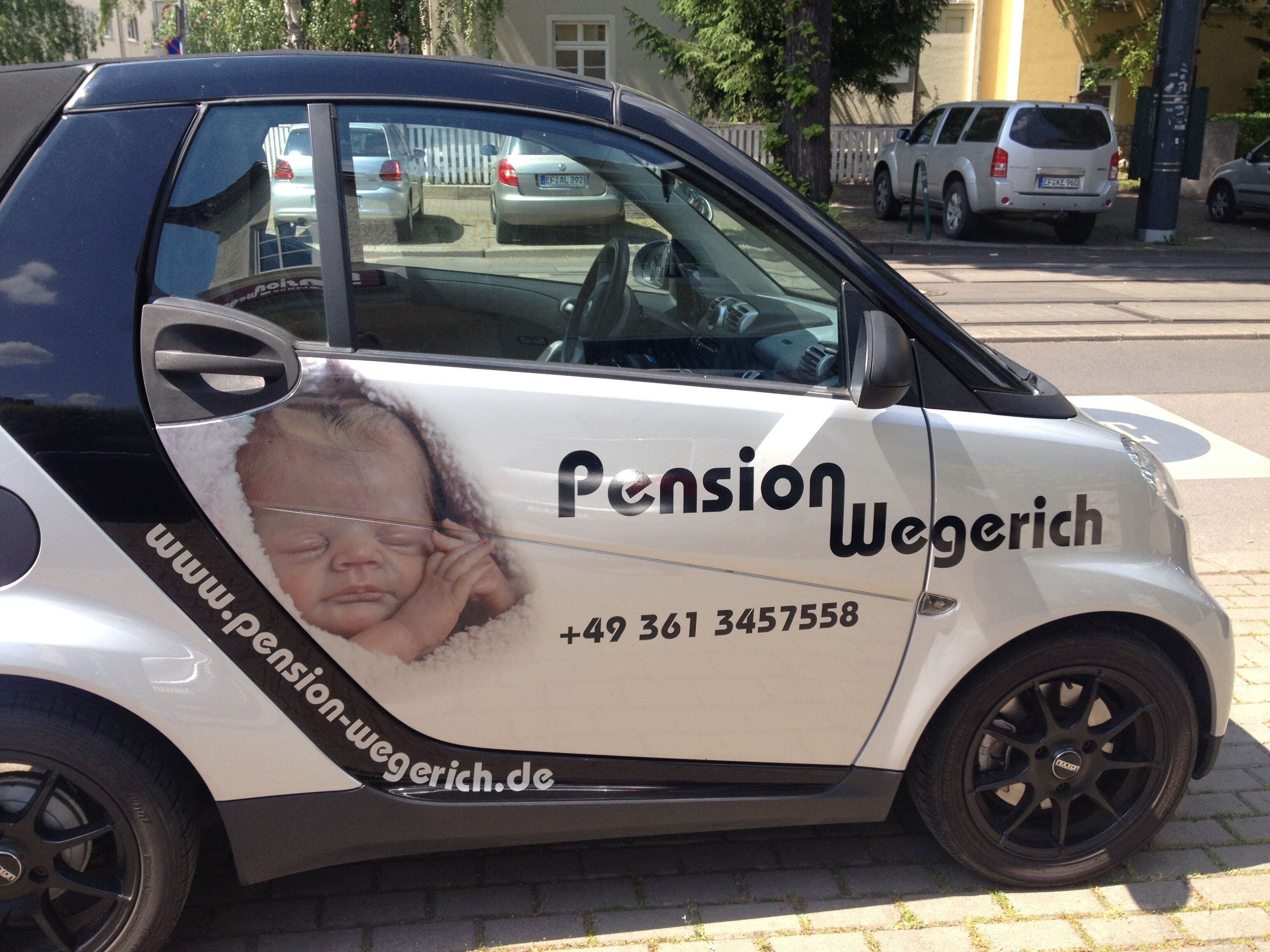 A white car with a side advertisement for Pension Wegerich, including a website and phone number.