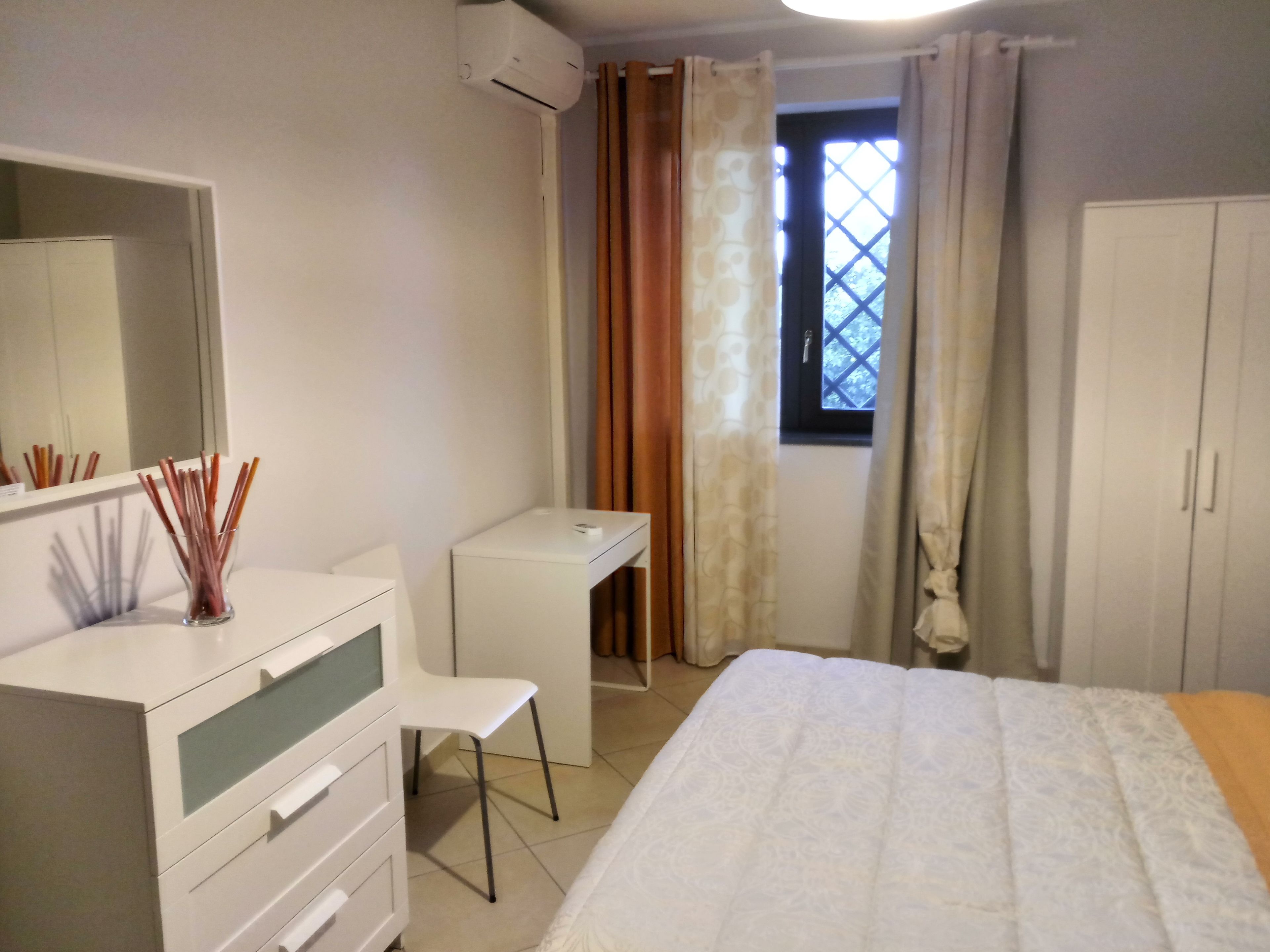 A bedroom with a bed, a desk, a chair, a wardrobe, and a window with curtains.