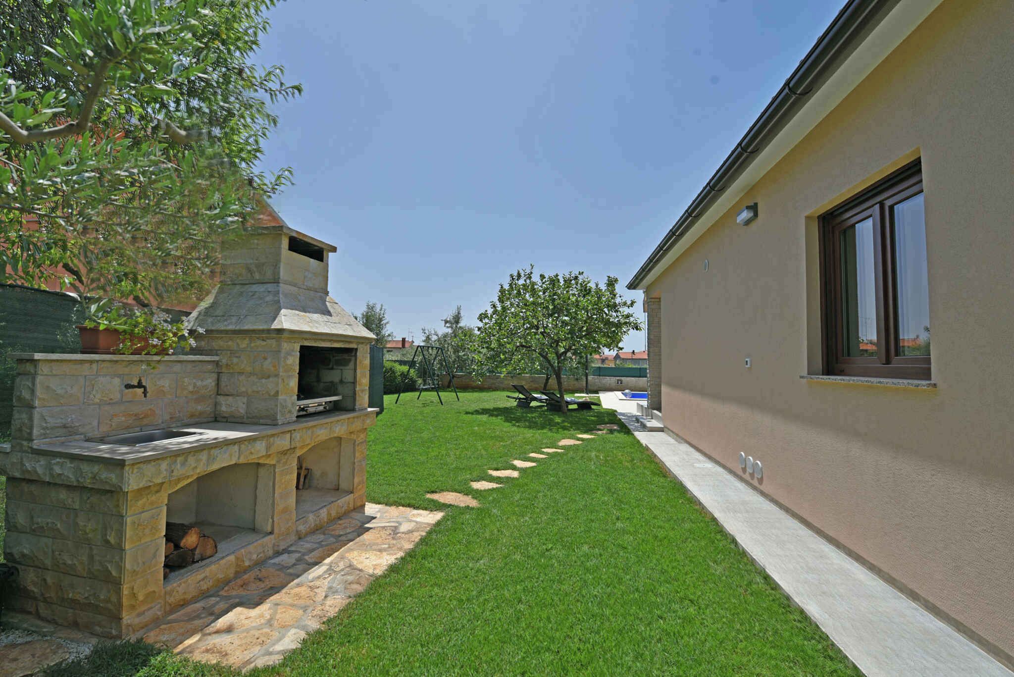 Un jardin avec un espace barbecue en pierre, une pelouse et une maison.