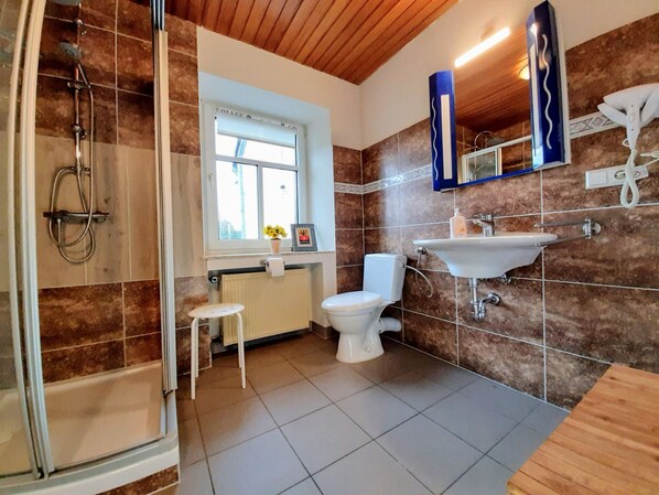 Un baño con ducha, inodoro, lavabo y un taburete pequeño.