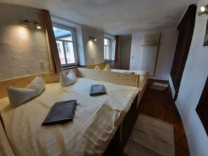 A compact hotel room with two single beds, a small window, and a radiator.