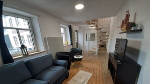 Una sala de estar moderna con un sofá gris, una mesita redonda, un mueble para la televisión y una escalera de madera.