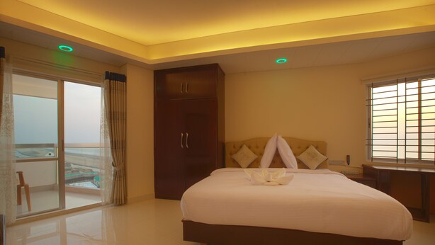 A hotel room with a large bed, a wardrobe, a desk, and a balcony with a view. - Exotica Sampan (Cox's Bazar)