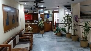 Un vestíbulo de hotel con mostrador de recepción, zona de estar, ventiladores de techo y plantas en macetas.
