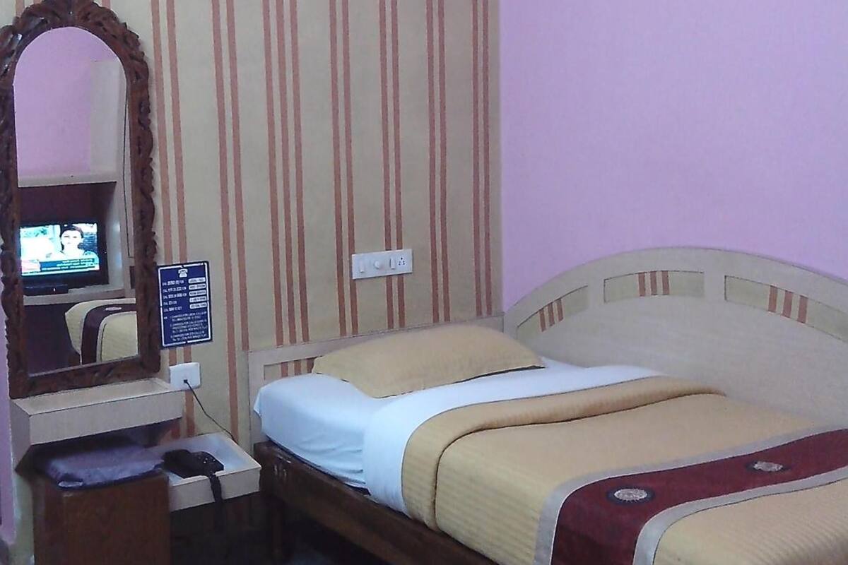 Une chambre d’hôtel avec un lit, un bureau avec une télévision, un miroir et un sol à motifs.