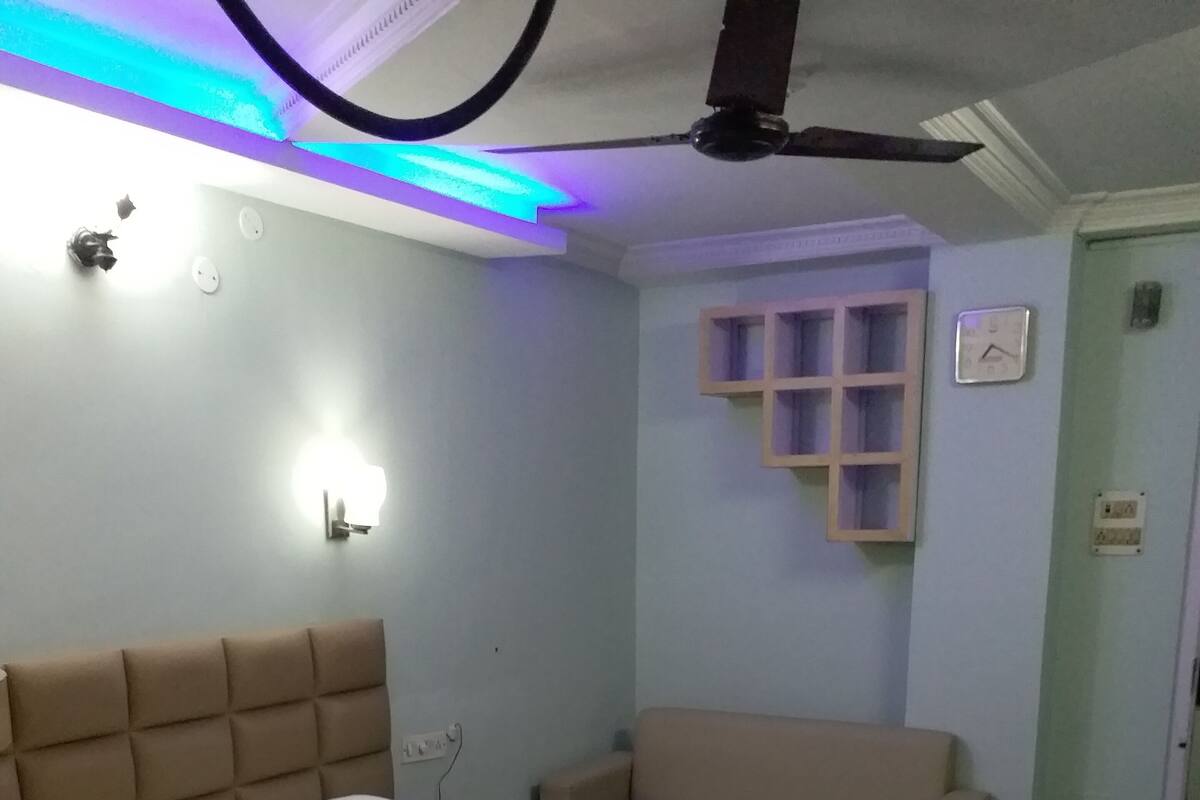 Une chambre avec un grand lit, une table de chevet, un ventilateur de plafond et un luminaire fixé au mur.