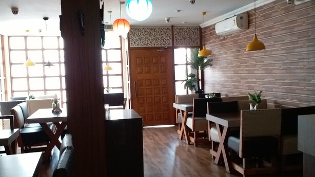Interior de restaurante con suelo de madera, mesas y sillas. Se observan luces colgantes y una gran lámpara decorativa.
