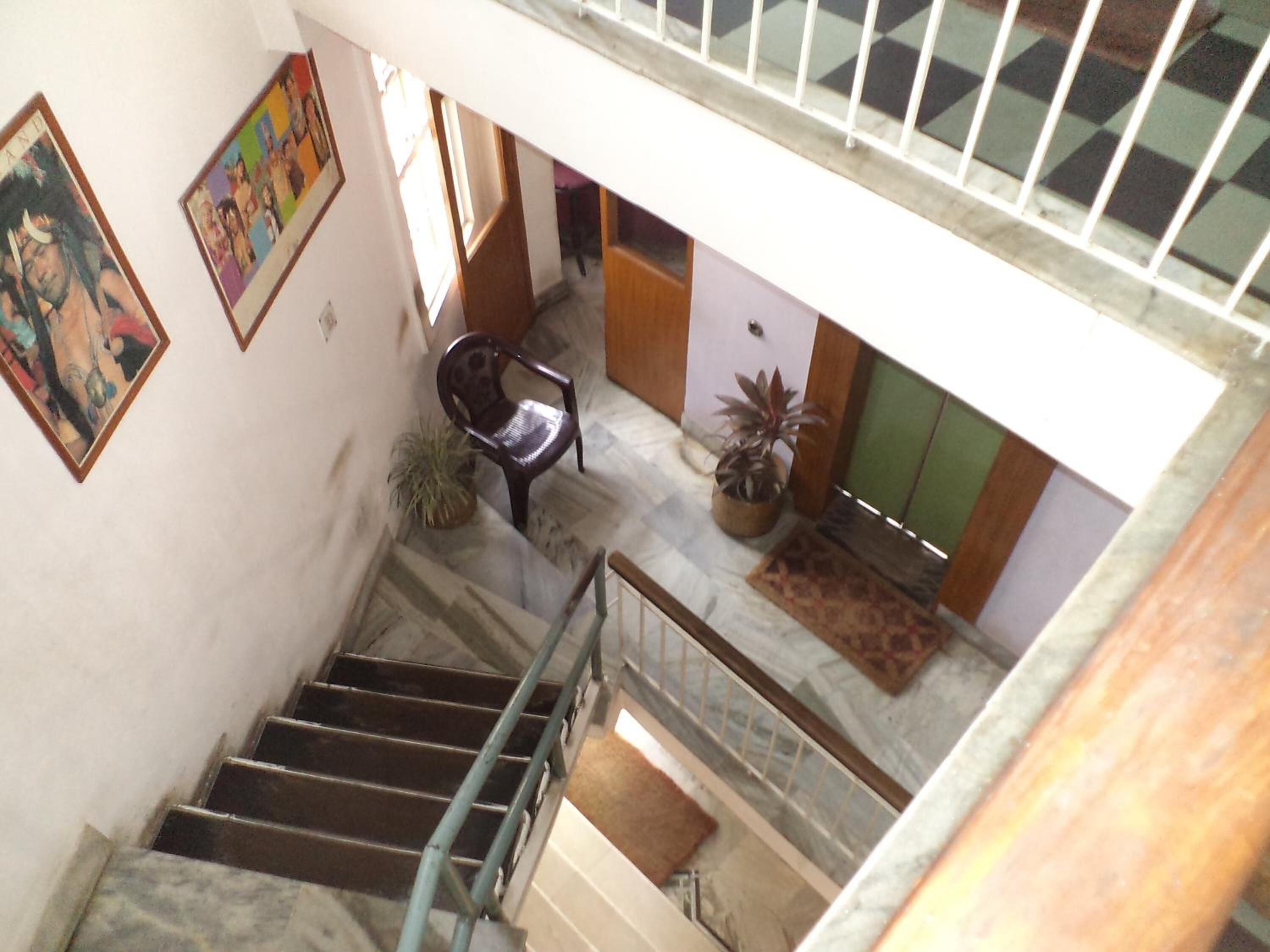 A staircase with a metal railing, leading to a lower level. There are potted plants on the landing and a chair in the middle of the space.