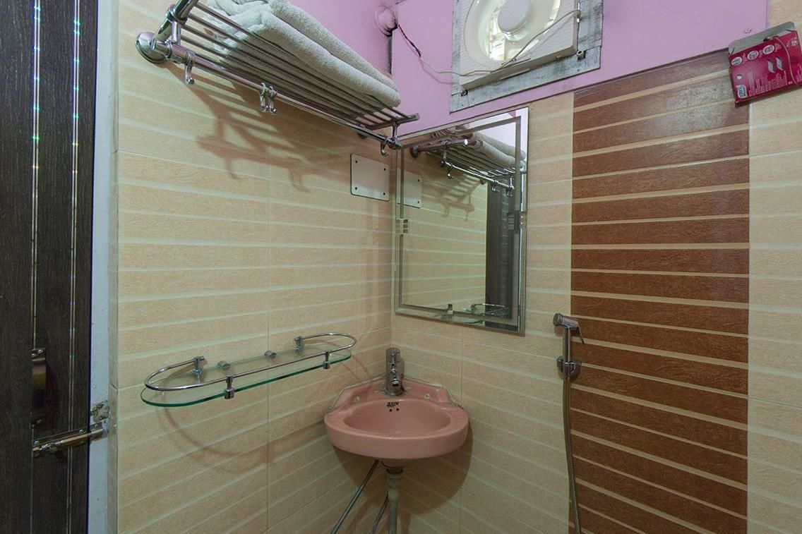 Un baño con un lavamanos rosa, un estante de vidrio, un perchero y un espejo.