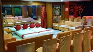 Habitación de hotel con una cama curvada, varias zonas de estar y un escenario con palmeras.