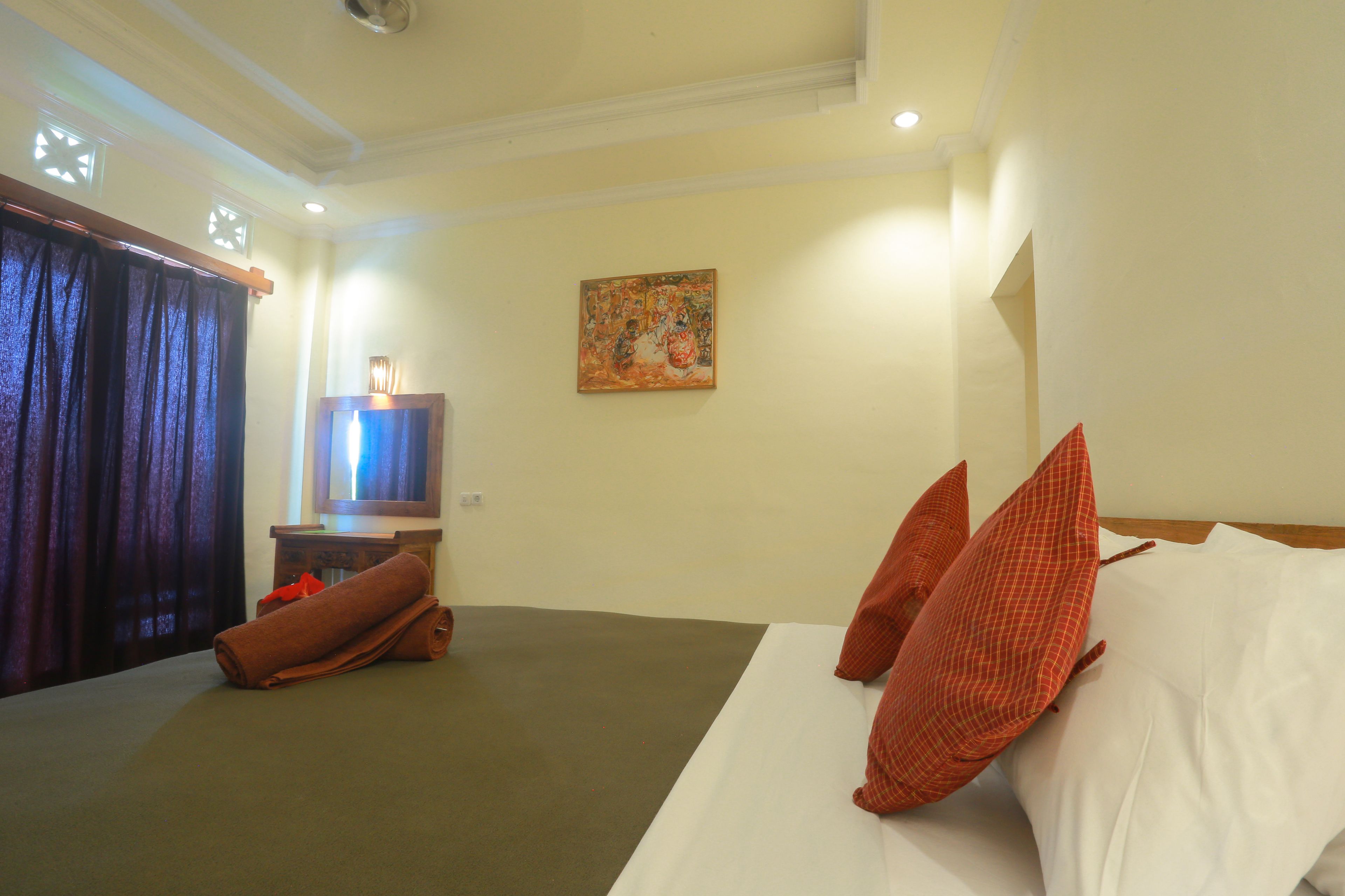 A hotel room with a bed, pillows, a television, and a painting on the wall.