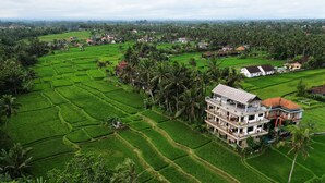 A large, multi-story building with a flat roof, surrounded by lush green rice paddies and palm trees. - Nirwa Ubud Karma (Ubud)