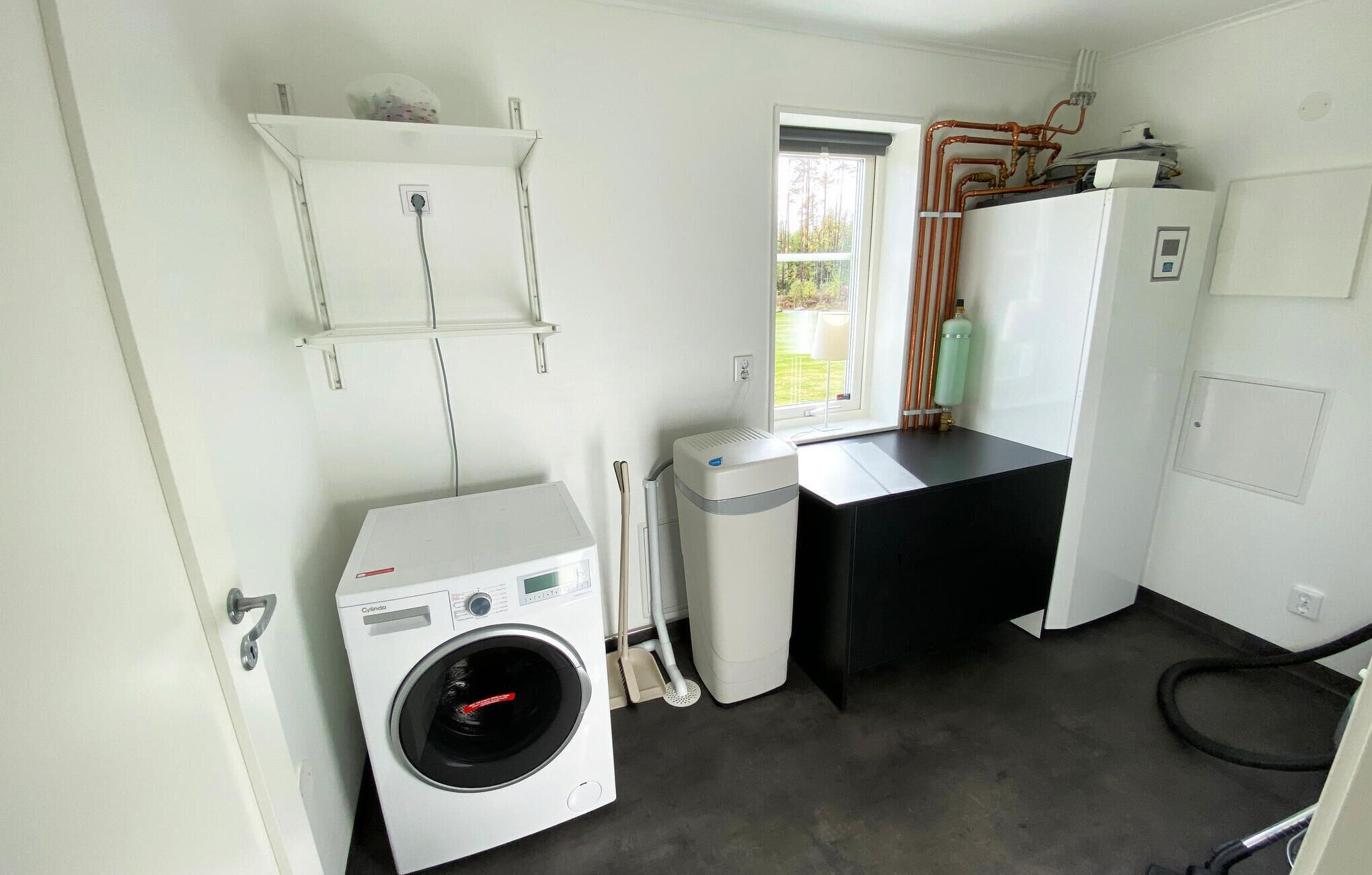 A laundry room with a front-loading washing machine, a dryer, and a small table with a water heater and a bottle of cleaning solution.