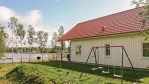 A house with a red-tiled roof, a swing set, and a grassy yard.