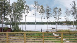 A wooden deck with a view of a lake, surrounded by birch trees and a distant shoreline with buildings.