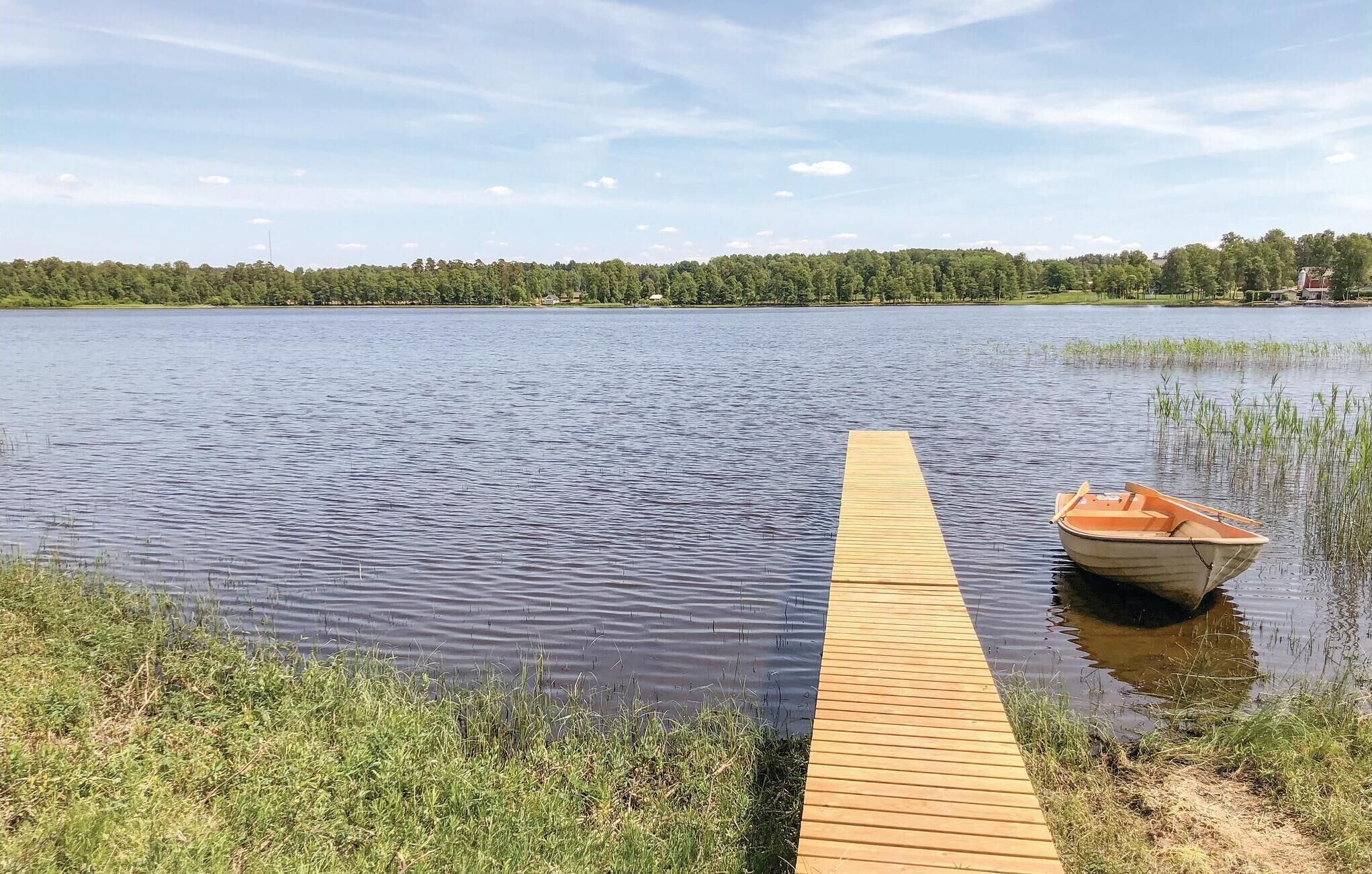 A wooden dock extending into a calm lake with a small boat docked at the end.