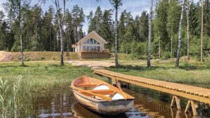 A wooden boat docked at a wooden pier leading to a cabin in a forested area.