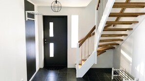 A modern interior with a black door, a staircase with wooden steps, and a hanging light fixture.