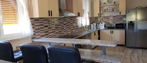 A modern kitchen with a central island, bar stools, and a refrigerator.